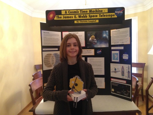Charlotte Campbell with a paper model she made of the Webb as well as a tri-fold board presentation for grade 6.