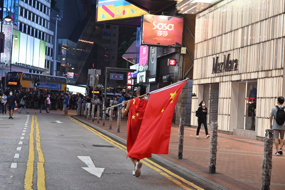 Local internet celebrity Haklam Lam strolls by, draped in a PRC flag and carrying a second one to "celebrate" this day.