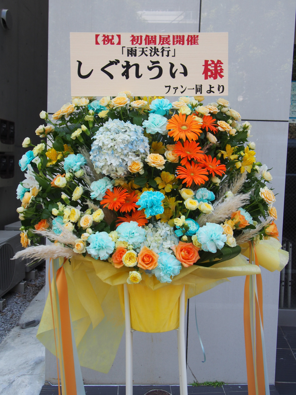 しぐれういお祝い企画 Mapart 寄せ書き 本日お花の方を納品致しました 黄色メインに柔らかなオレンジと赤橙色 青色を合わせ アクセントにリボン お花の種類はガーベラ アジサイ バラなど フラワースタンドを製作頂きましたのはフローリストカノ