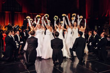 The dancing couples with their outfits and the air of a formal dance remind me of debutante balls, which are about making a debut in the world and showing off young adults in high society - it's not really a loving/fun dance. He's just waiting in a world of pretenses.