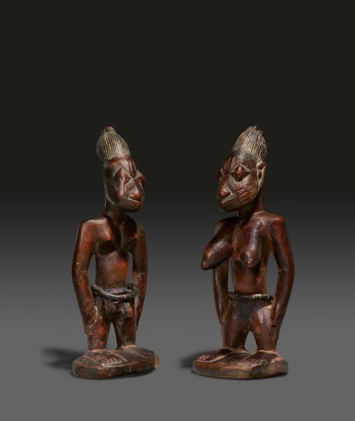 The completed ibeji figure is carved as an adult, rather than as the deceased infant, in a mythological form that depicts the concentrated calm of a Yoruba artist. When the carving is completed, the artist is given a feast and payment as determined by the Orishas.