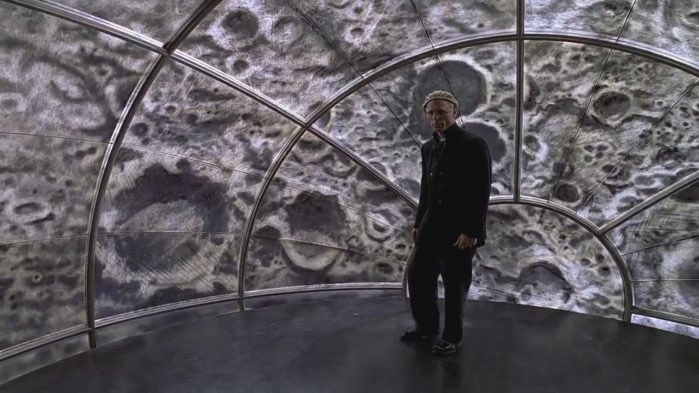 In The Truman Show, the protagonist unknowingly goes about his daily life on the set of a reality tv show. At the end, he ends up finding the exit door of his artificial world and discovers the director, who has been orchestrating his life from a watchtower disguised as the Moon.