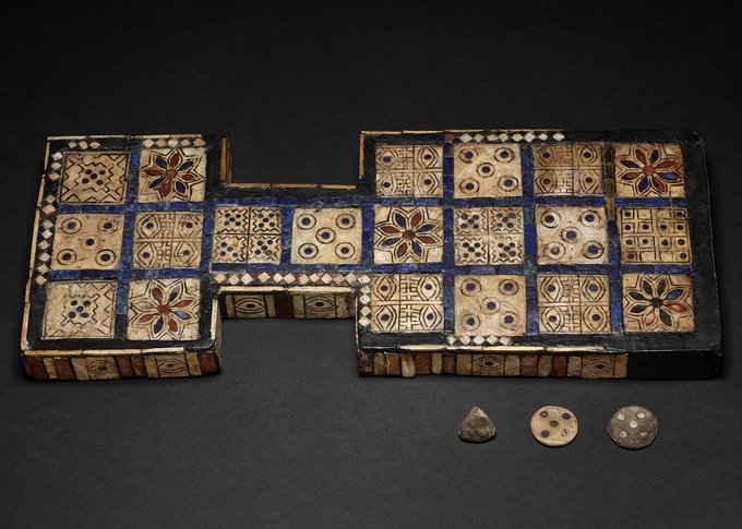 A wooden game-board with an inlaid face with 20 squares, some sculptured with an eye and some possibly with rosettes.