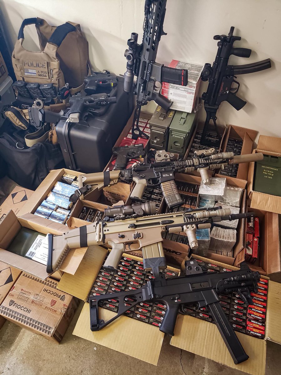 Sometimes, even though he has a six-year-old boy, Jon stages his unsecured rifles and handguns with open boxes of ammunition so he can photograph them with his... What's that in the corner? A chest rig with patches? What do those patches say about him?