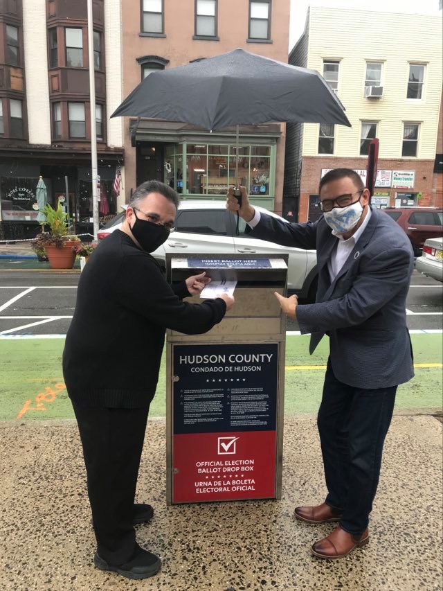 countyclerkhc's tweet photo. Neither rain nor snow nor sleet can stop City Clerk Sean J Gallagher from casting his vote while County Clerk Junior Maldonado helps keep him dry. You too, can drop off your ballot at City Hall located at 280 Grove Street in Jersey City. #HCVOTE2020 https://t.co/LlvRqReJbg