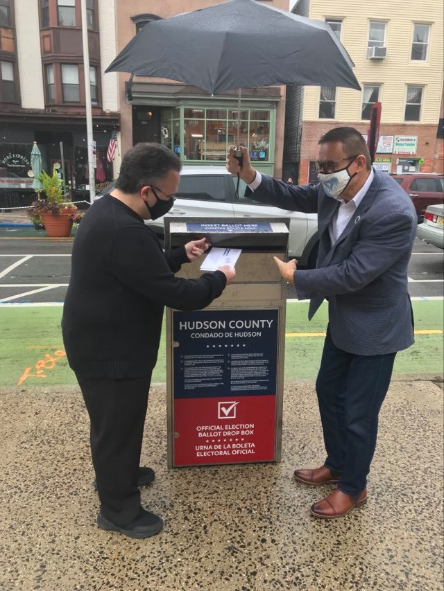 countyclerkhc's tweet photo. Neither rain nor snow nor sleet can stop City Clerk Sean J Gallagher from casting his vote while County Clerk Junior Maldonado helps keep him dry. You too, can drop off your ballot at City Hall located at 280 Grove Street in Jersey City. #HCVOTE2020 https://t.co/LlvRqReJbg