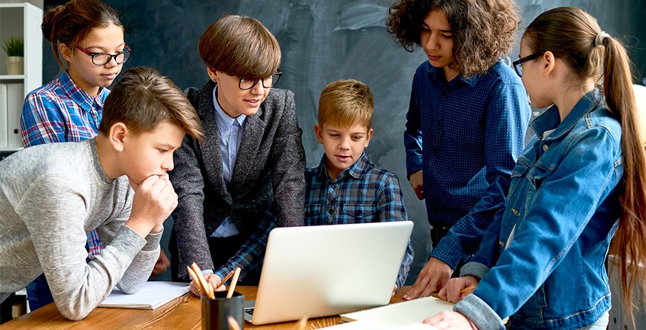 a group of children gathered around a laptop
