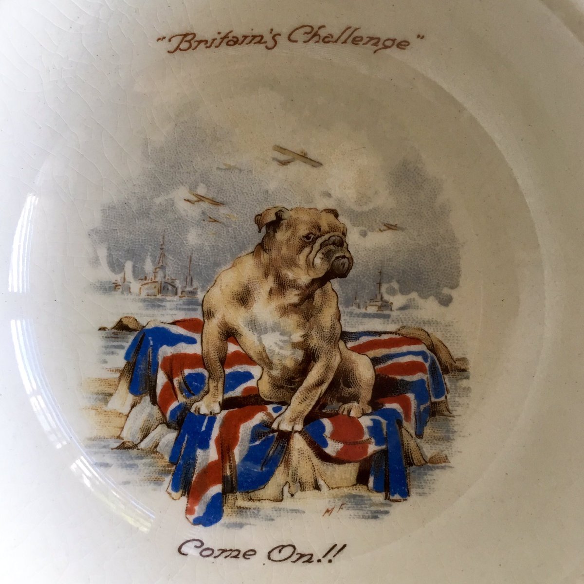 A closer look at my new baby plates reveal itty-bitty ships and aircraft. What the British bulldog is doing sitting on a rock draped in the Union Jack in the middle of the sea is anyone’s guess. Perhaps it is, as the text suggests, a challenge.