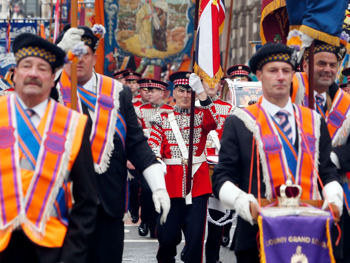 ¿Por qué? El gesto de tocar la flauta, hace referencia a “The Orange Walk”. Un grupo de unionistas, protestantes que todos los años marchan en un desfile cuasi-militar-patriótico, por barrios de Irlanda del Norte, donde siempre termina en atentados, apuñalamientos, etc.