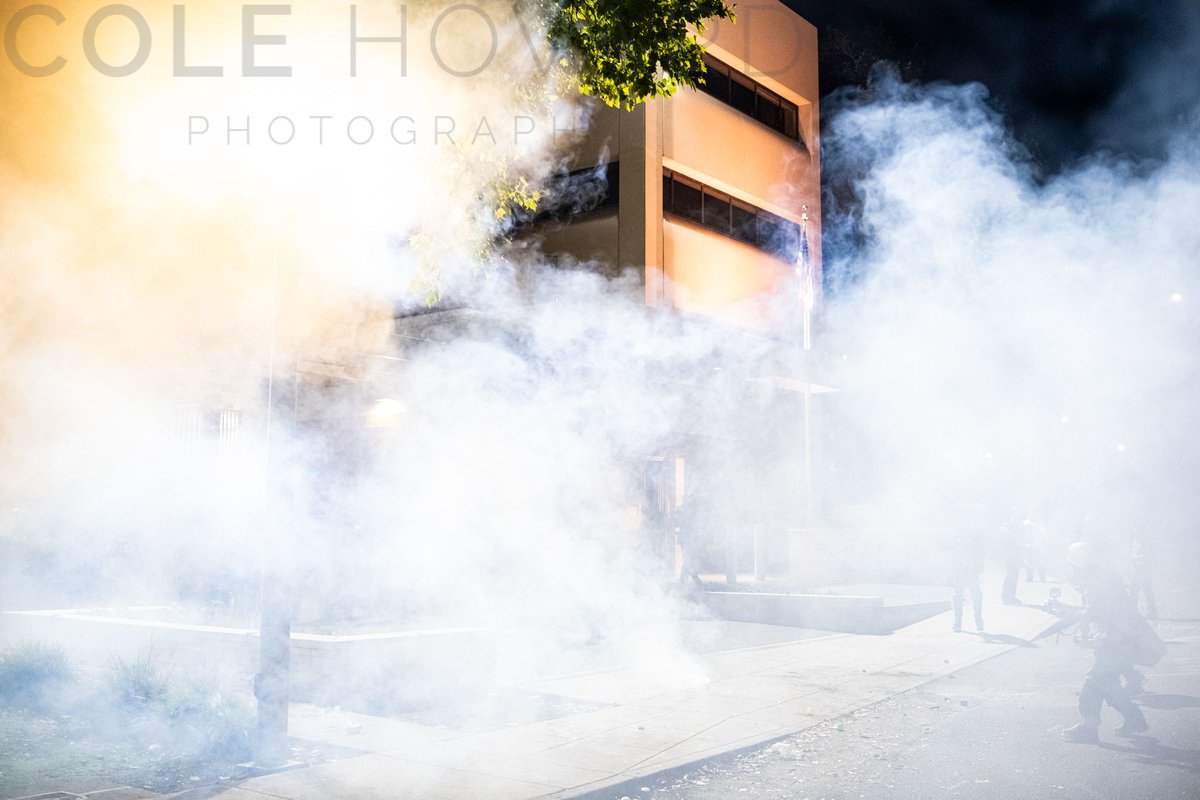 An American flag limply droops on the flag pole in front of the ICE building as it is engulfed in CS gas. This was one of the many moments when this chemical gas blanketed blocks of a neighborhood alongside multiple residential communities. #PortlandProtests #PDXprotest #BLM