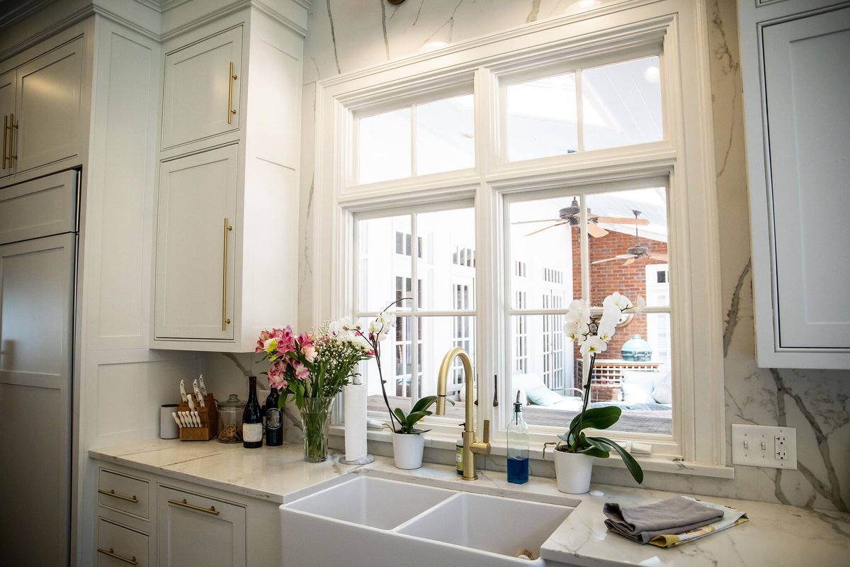 The color palette in this kitchen includes grays pulled from the marble countertops and stainless steel appliances and brass cabinet hardware that complements the gold tones in the travertine flooring. #kitchedesign