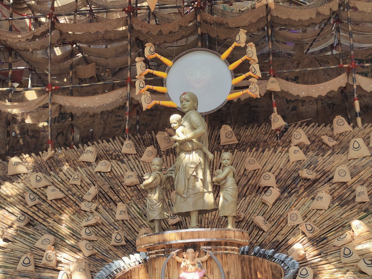 The pandal is decorated with jute bags that have 'traan' written on them, losely translated to relief/aid. Maa, instead of the traditional astras, is carrying traan.