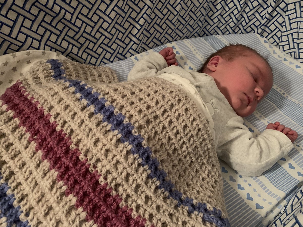 Baby sleeping in a crib under a knitted blanket