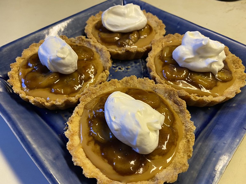Four mini dulce de leche tarts with caramel-rum bananas and whipped cream