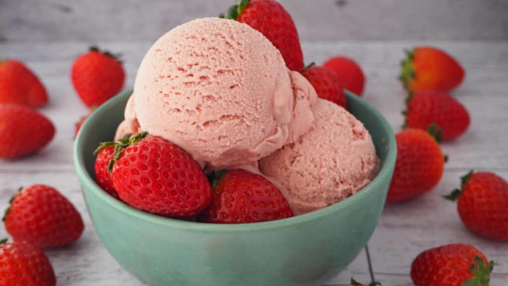 Strawberry ice cream in a bowl with fresh strawberries. 