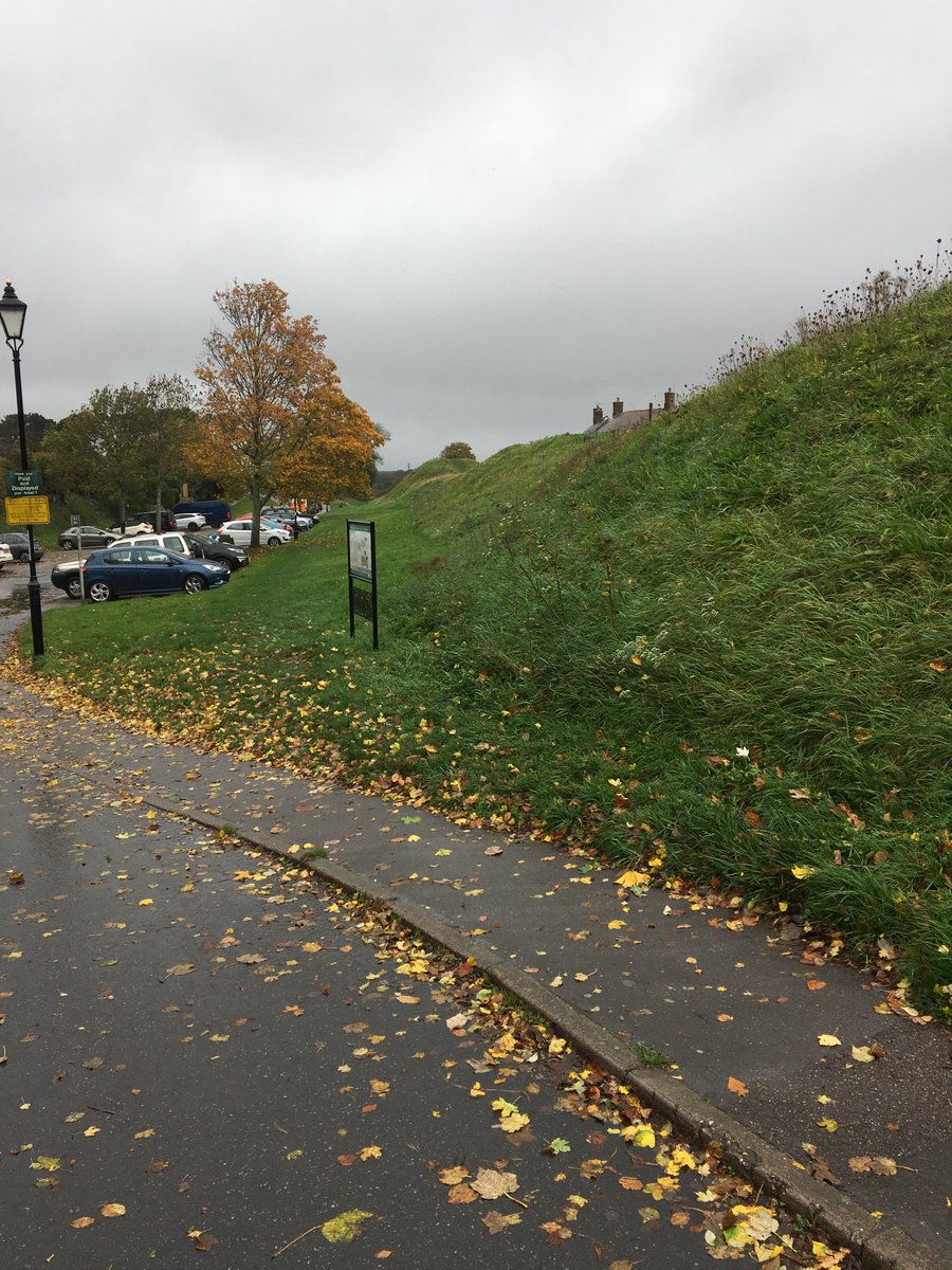 The earthwork banks survive up to 3 metres in many places, as here on the west side, where the cars provide some comparison. The car park lies at the bottom of what would once have been the ditch