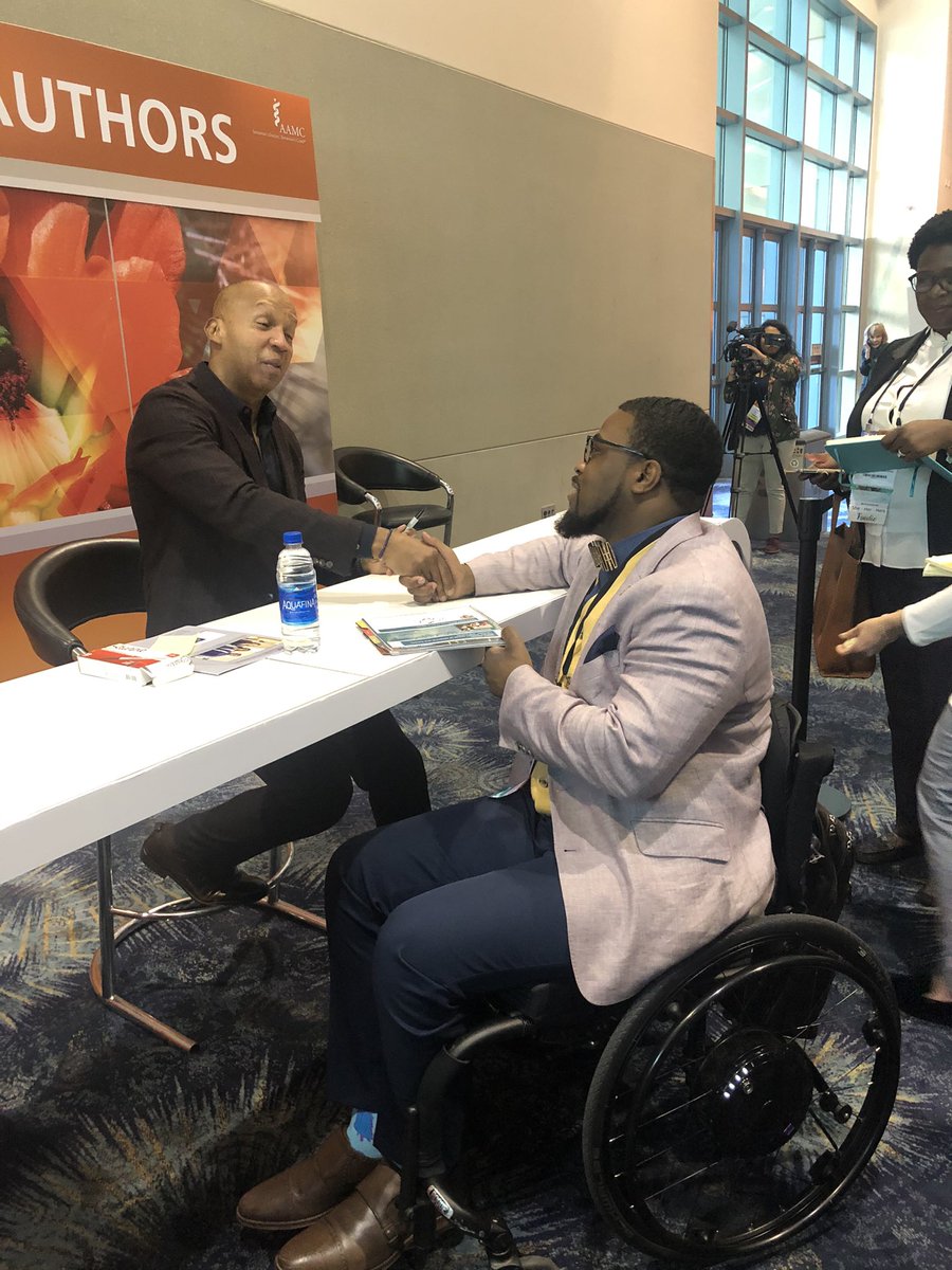 Man sitting in a wheelchair shaking hands with Bryan Stevenson across a table.