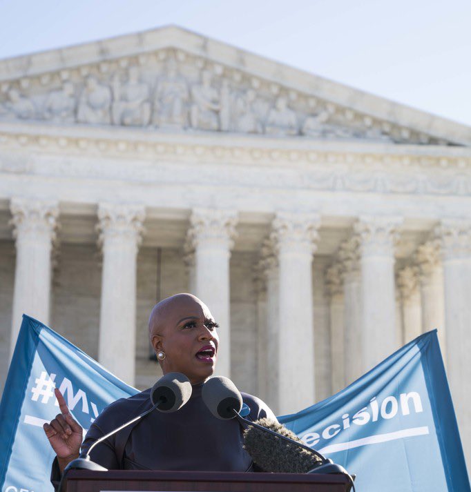 Ayanna Pressley speaks in front of the Supreme Court with a blue banner behind her.