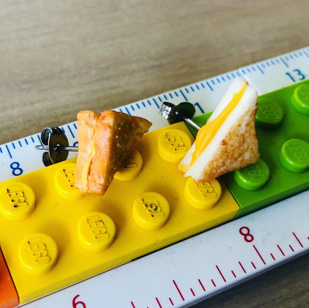 A close up of the cheese toastie earrings sitting on a LEGO ruler.