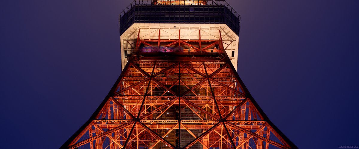 Photography by Liam Wong of Tokyo tower at night. A wide cinematic frame of Tokyo tower showing its detail. The sky is purple and the tower is orange in color. The design looks similar to Eiffel Tower in Paris.