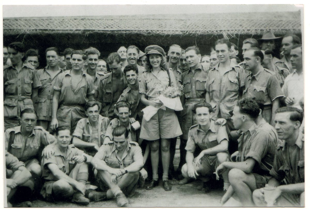 Here's a picture of Vera Lynn in Burma, holding a bouquet of flowers and with her big smile. Does anyone know any of the names or history of any of the soldiers in this photo? #KeepSmilingThrough VeraLynn.lnk.to/KeepSmilingThr…