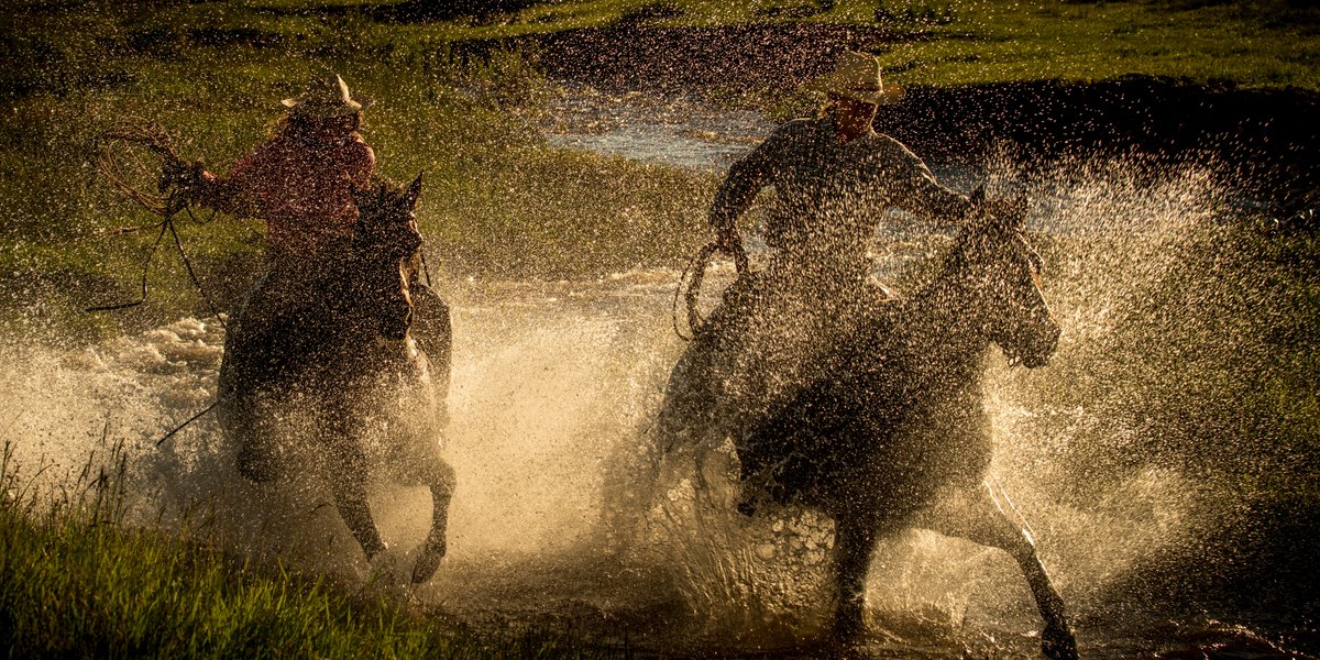 Photo by Dan Ballard of two horse riders crossing a small body of water and splashing water drops high in the air.