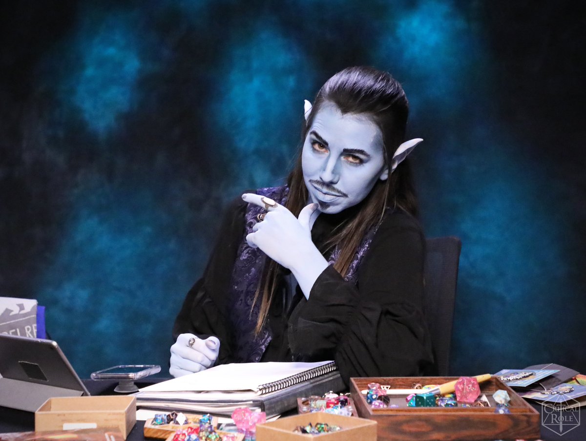 Laura Bailey is dressed as the Gentleman. Her skin is the same blue as Jesters with the goatee wearing a black shirt. She smoulders