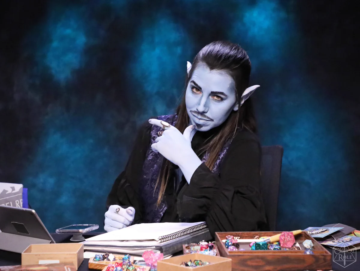 Laura Bailey is dressed as the Gentleman. Her skin is the same blue as Jesters with the goatee wearing a black shirt. She smoulders
