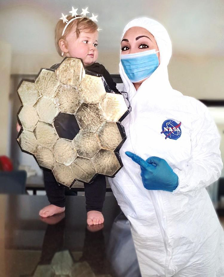 Kellie Gerardi in a NASA cleanroom suit with her baby in a James Webb Space Telescope primary mirror costume