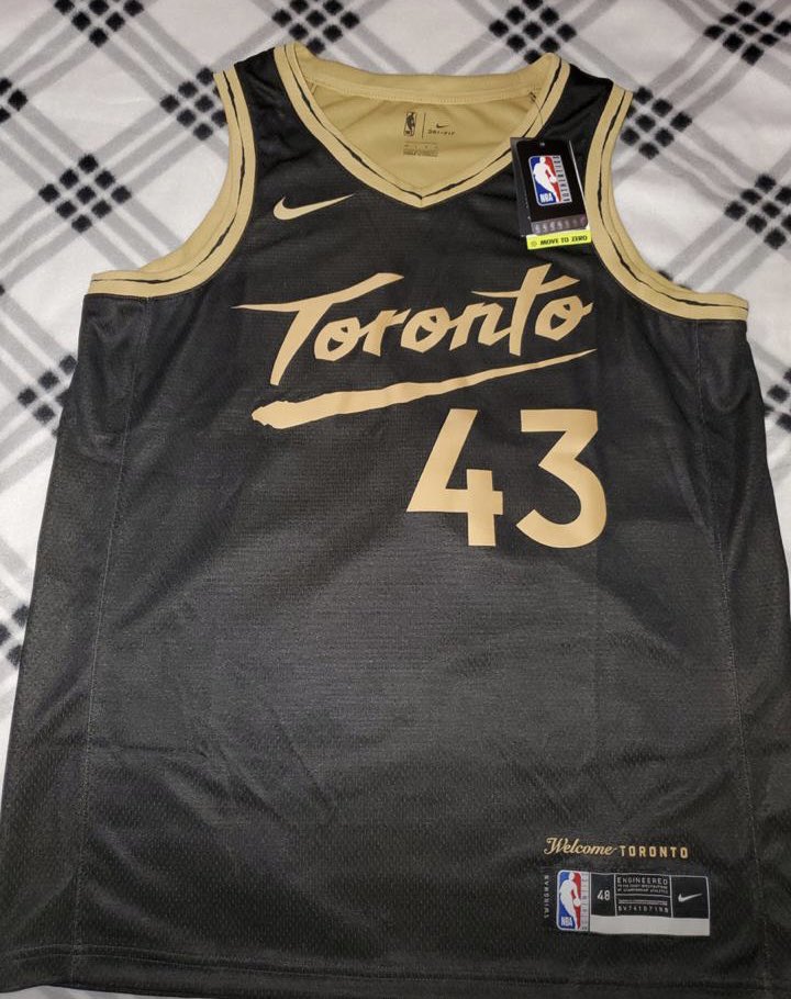 Chemise noire des Toronto Raptors.  Elle est sur une table.  Le nom Toronto et le nombre 43 sont en or.