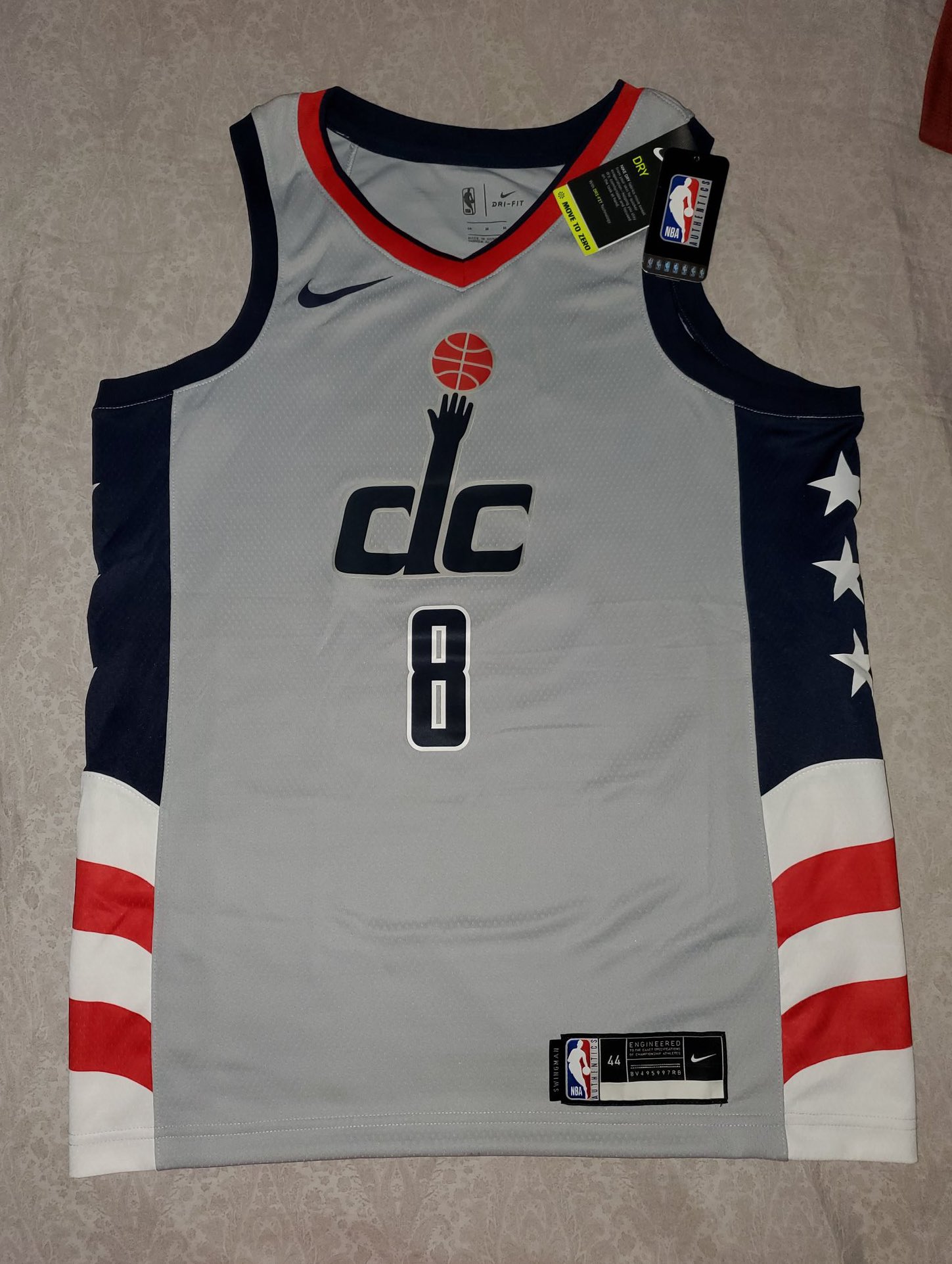 Chemise grise de Washington Wizards sur une table.  Il porte le numéro 8, le logo DC sur la poitrine et des détails du drapeau des États-Unis sur les côtés.