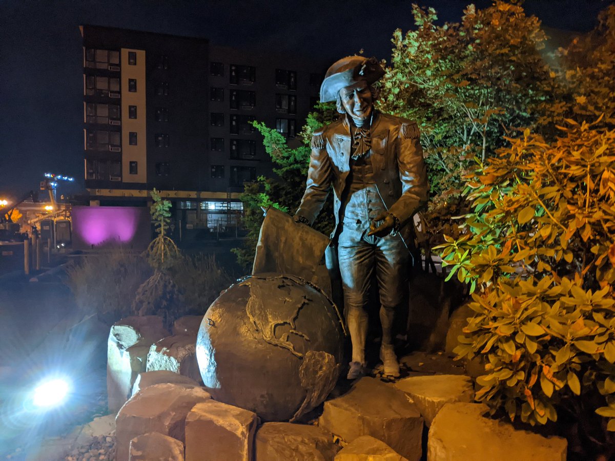 A statue of a smiling man in a tricorner hat and other colonialist clothes pointing at a globe and smiling