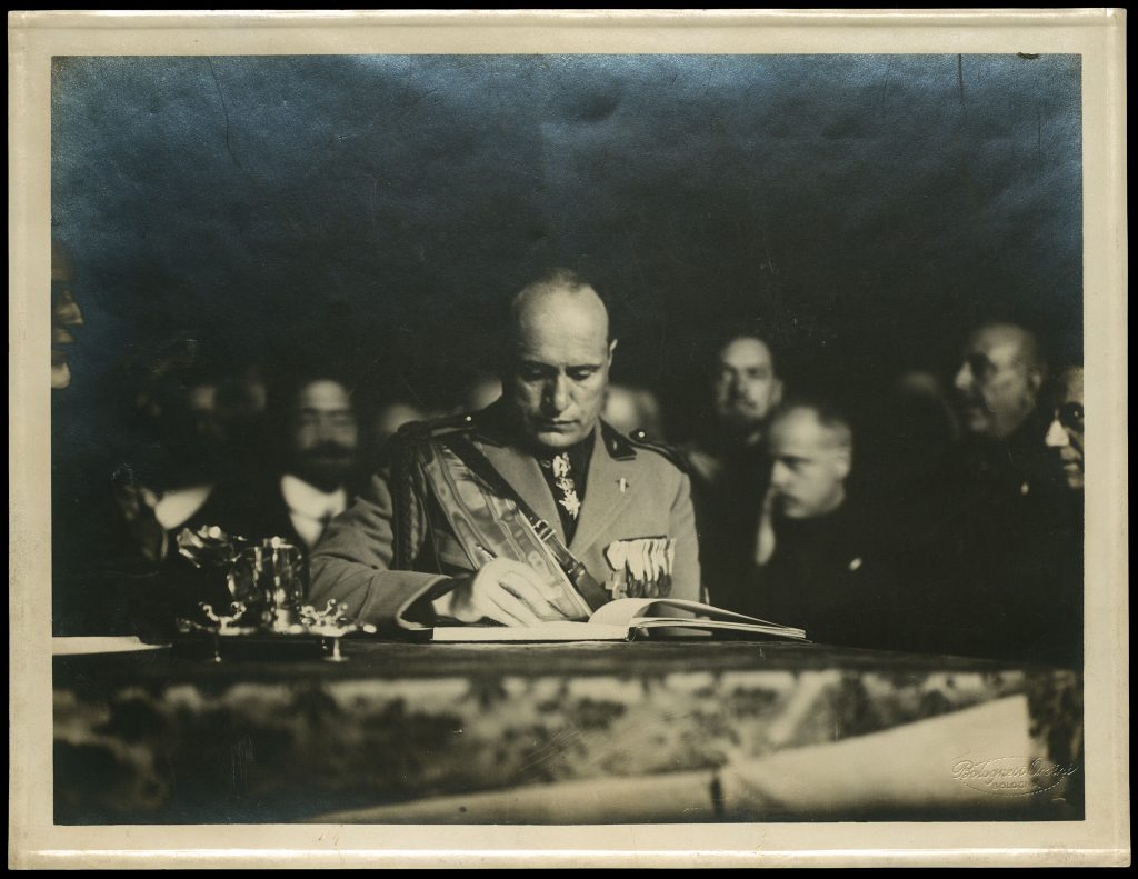 After the ceremony, Mussolini heads to the Archiginnasio Library, where he signs his name in the Visitors' Book (photo). He then climbs into a red open-top Alfa Romeo to be driven along the streets lined with cheering crowds to the station for his return to Rome >> 9