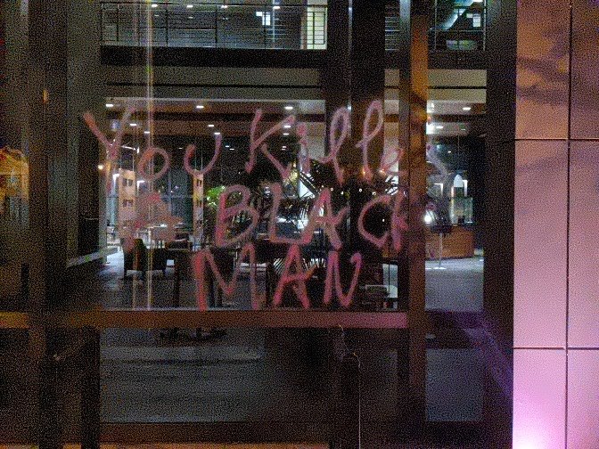 Spray paint on a window that reads "You killed a black man"
