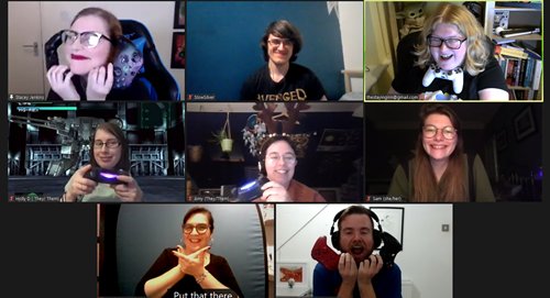 A zoom call of people, lots are holding up gaming controllers laughing and smiling.