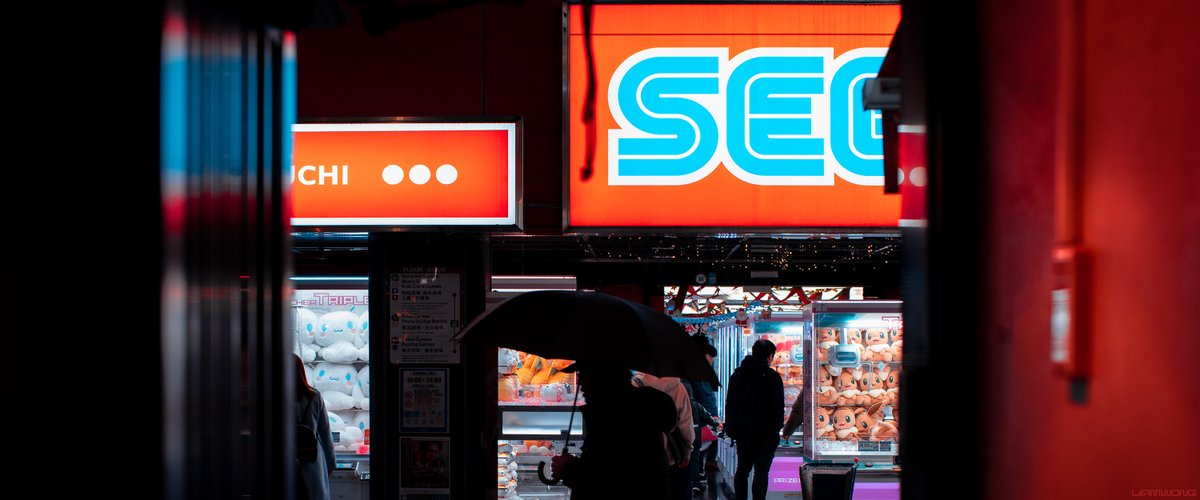 Photography by Liam Wong of Japan at night. A man walks through an alley - the SEGA logo can be seen overhead.
