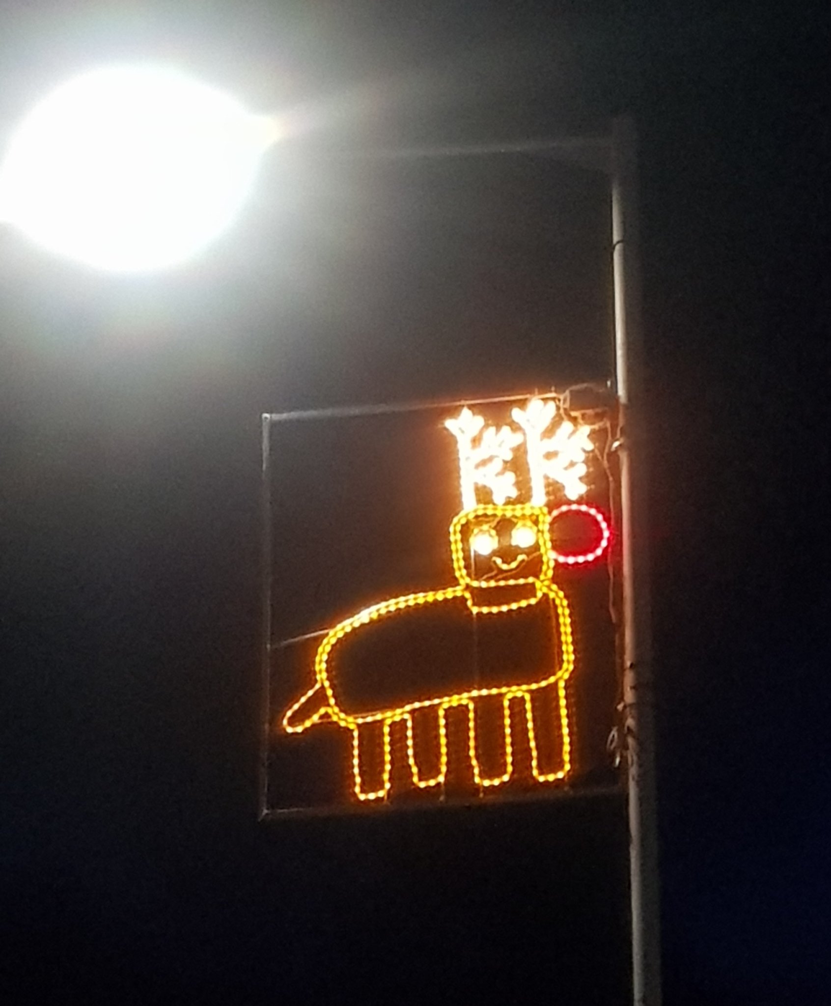 A photo of a city's Christmas lights on a light pole, in the shape of a child's drawing of a reindeer