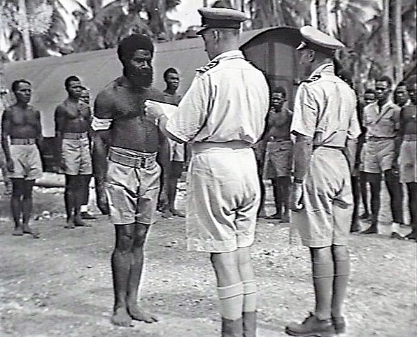 Oct 1943 Guadalcanal: Lt Cdr Pryce-Jones, Intelligence Officer, Naval Intelligence Division, R.A.N. (responsible for Coastwatchers), presents the Loyal Services Medal to Sergeant Yauwiga.He was credited for showing remarkable bravery and his positive influence on local people.