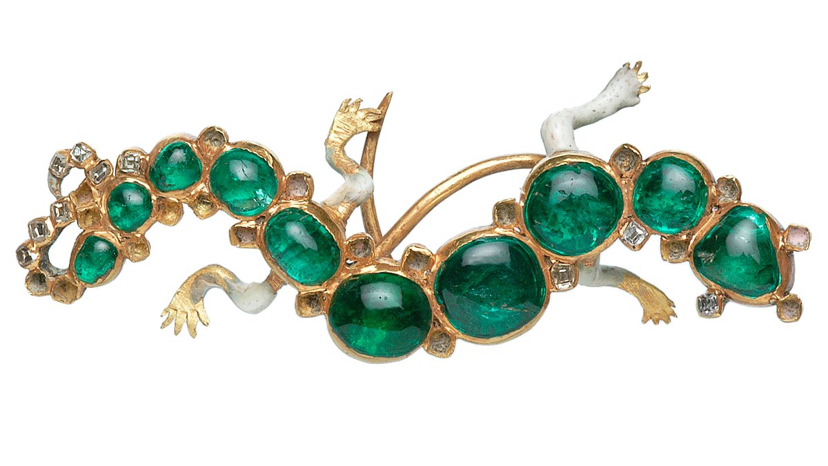 A gold, enamel and gem-set brooch in the form of a salamander with splayed limbs, raised head, gaping mouth and tightly curled tail. The sinuous body is fashioned from ten cabochon emeralds flanked by 30 table-cut diamonds (20 missing).