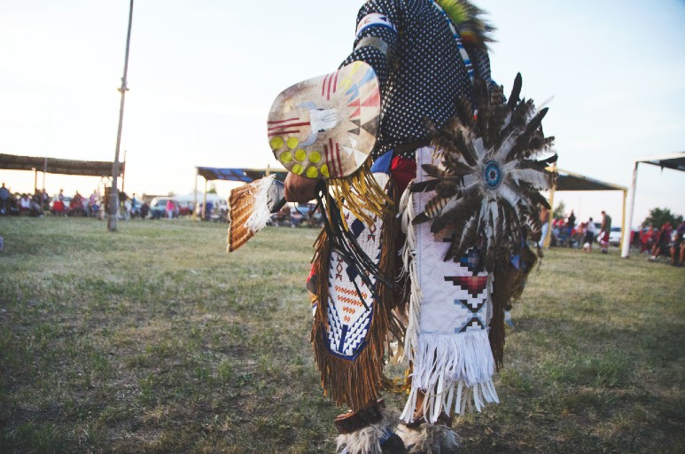 a photograph of a man dressed in a full Native American regalia at a pow pow