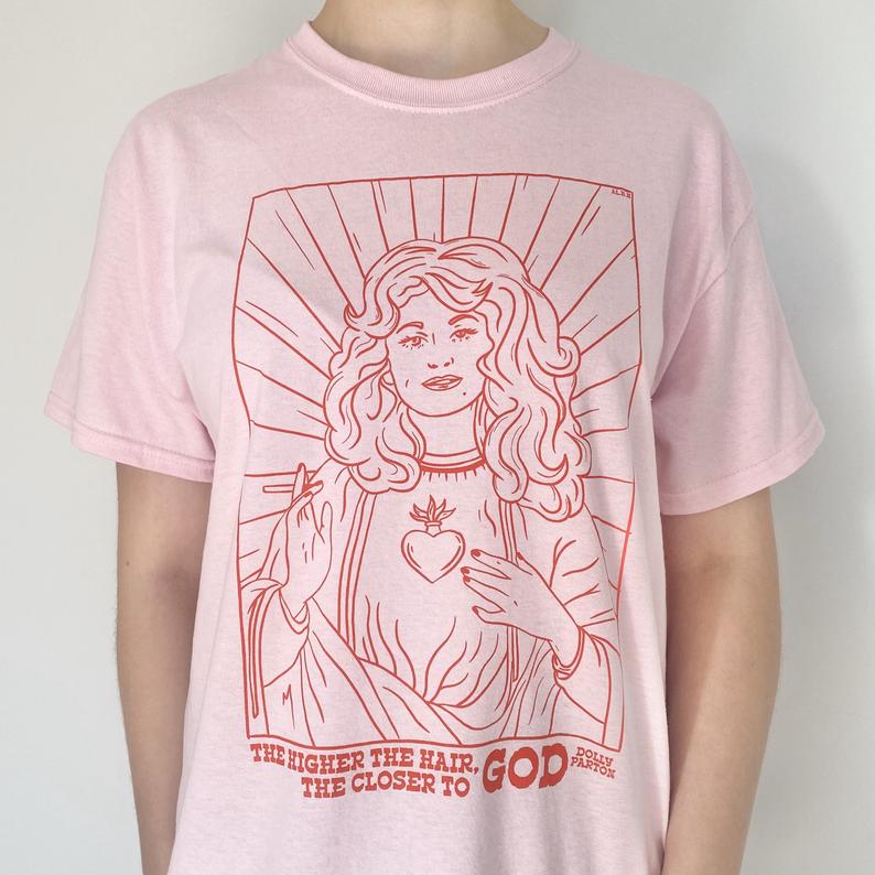 LYDVENT DAY 3: There's only one big-haired blonde I want running America! If you know a fellow fan of Ms. Parton, they'll love finding a Dolly tee under their treeDolly Good Day:  https://tidd.ly/38zaEJd  (AFF)Saint Dolly:  https://tidd.ly/3eBLSsy  (AFF)