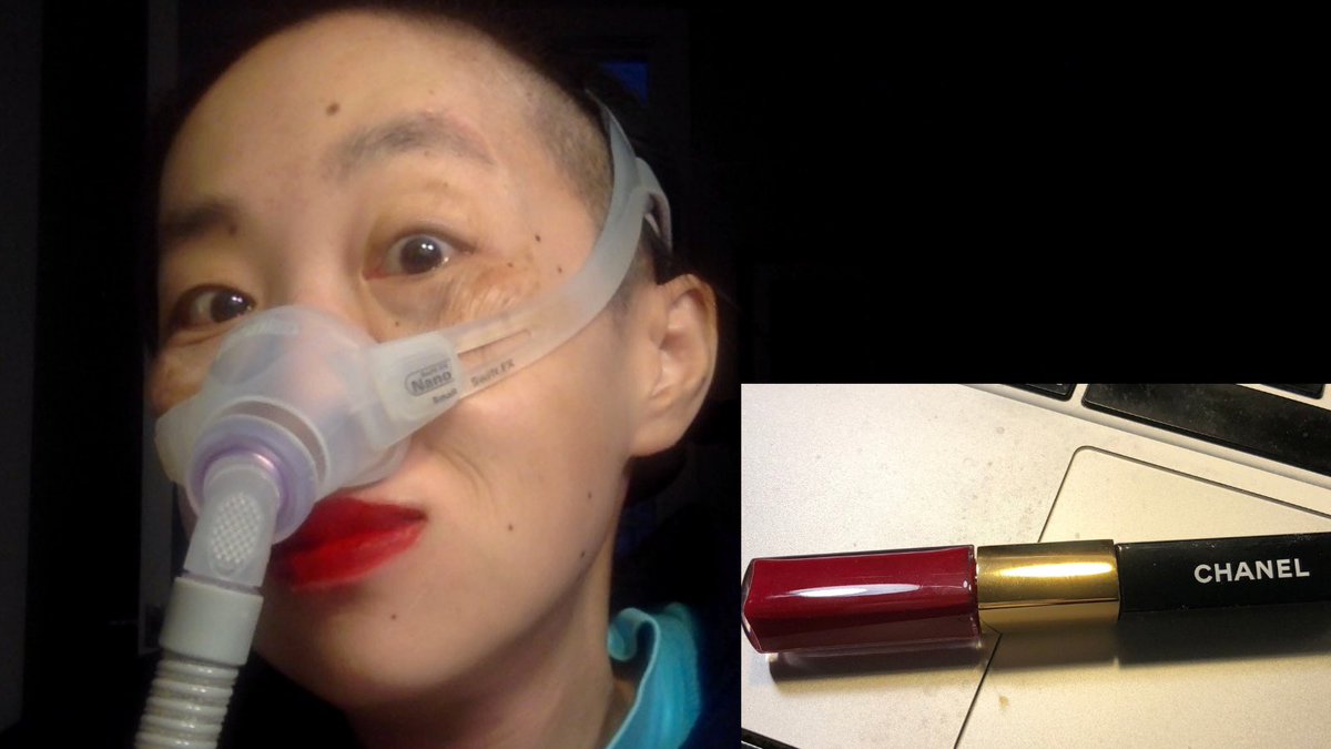 Asian American woman with a bright red lip color with short hair with a mask over her nose attached to a gray tube. On the lower right corner is a Chanel lip gloss. The background is black.