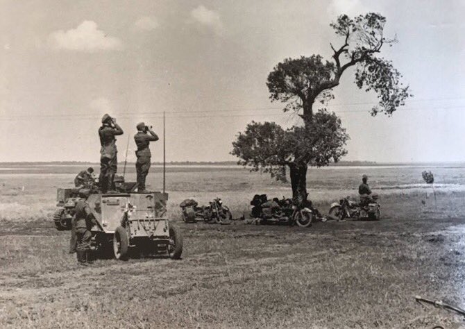 1942 Southern Russia c.Fall Blau.Btl C/O (right) of 119 Art.Rgt. 11 Pz Div & 3 Batterie O/C (left) stand on a Sdkfz 253, watching for shell fall on the horizon. Kradmeldern (despatch riders) are parked, ready to distribute orders.41a)