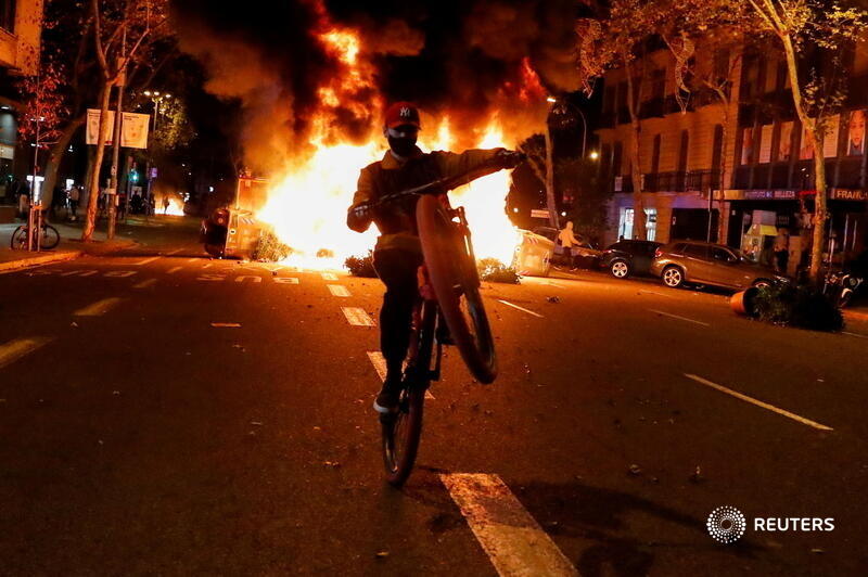 reuterspictures's tweet photo. A person rides a bicycle in front of a fire during a protest against the closure of bars and gyms, amidst the coronavirus outbreak, in Barcelona, Spain. More photos of the week: https://t.co/BCYpGgeT6L 📷 @NachoDoce12 https://t.co/Xvlr0stfuw
