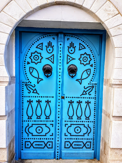 1) In Tunisia, if you look closely at details, you can find fish symbolism EVERYWHERE:Doors, jewelry, dresses, walls, windows, mosaics, songs, expressions "7outa 3lik" etc...Sometimes you can even find actual fish tails hanging around!Fish symbolizes fruitfulness and luck.