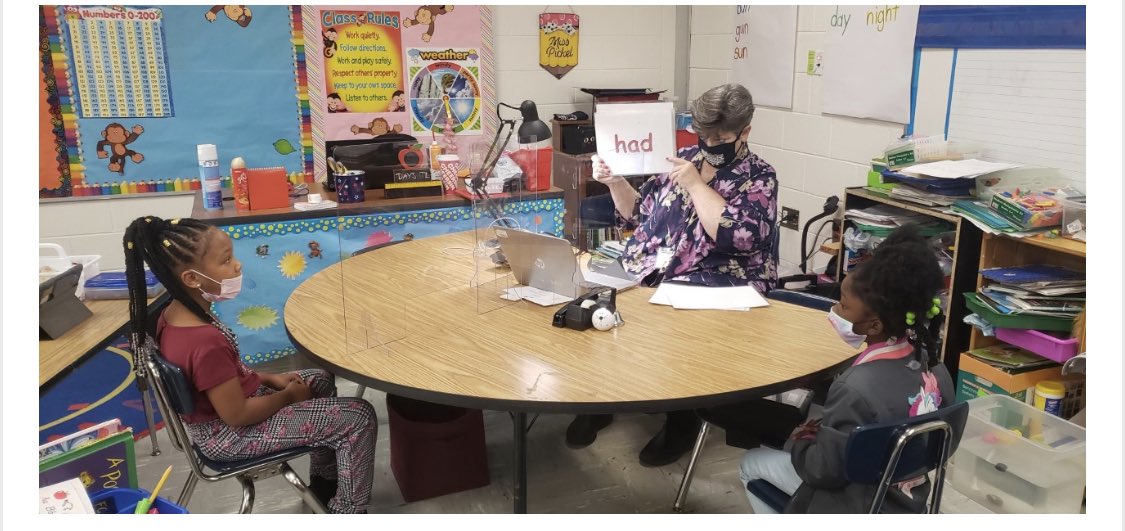 WLE_HCS's tweet photo. Kindergarten teacher, Ms. Pickel, is using a sneeze guard while working with a small group on sight words. #MaskUpHenry #SafetyFirst #DolphinNation🐬 https://t.co/AwZ7LiznAH