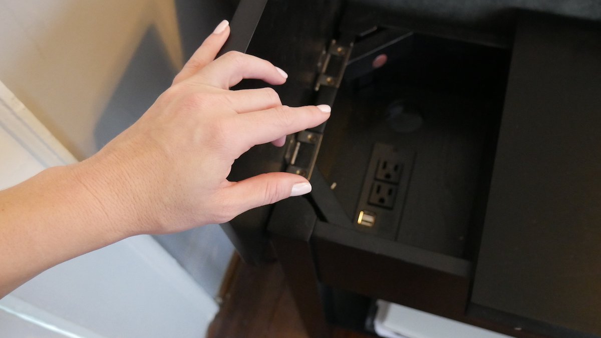 Image of my hand opening a secret compartment in a side table that has extra outlets for our cyborg convenience.