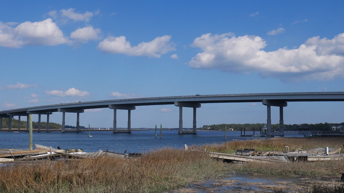 Image of a bridge from one part of an island to another part of an island. Sky with some clouds. Bunch of wreckage in front of the bridge.