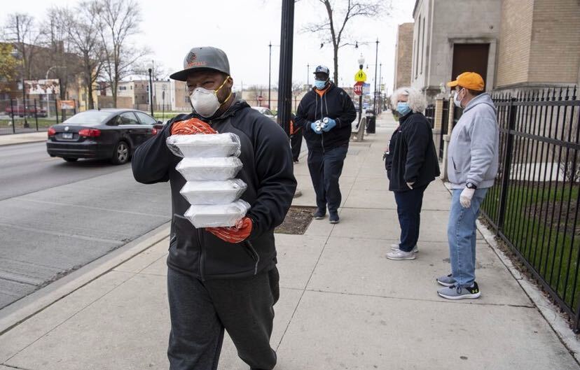 A person wearing a mask holding food that he's about to distribute