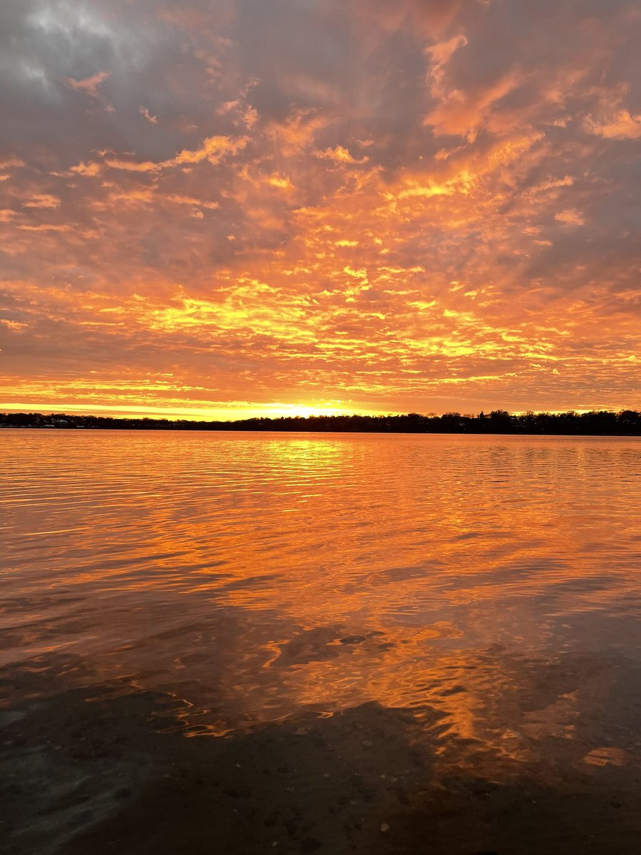 Orange and yellow vibrant sunset with reflections and ripples on Lake Harriet, Minneapolis. The horizon is a bright orange and the clouds textured, offer a nice array of  right orange to peach.